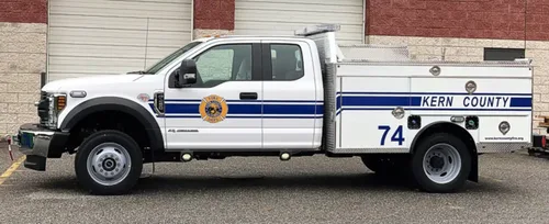 Exterior view of small fire truck showing cab, body compartments, and wheel/tire area.