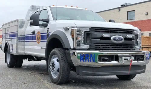 Exterior view of small fire truck showing cab, body compartments, and wheel/tire area.