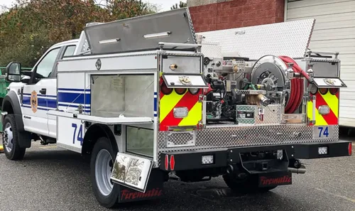 Exterior view of small fire truck showing cab, body compartments, and wheel/tire area.