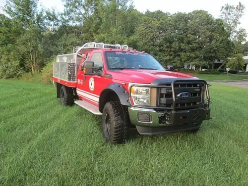 Exterior view of small fire truck showing cab, body compartments, and wheel/tire area.
