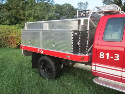 Exterior view of small fire truck showing cab, body compartments, and wheel/tire area.