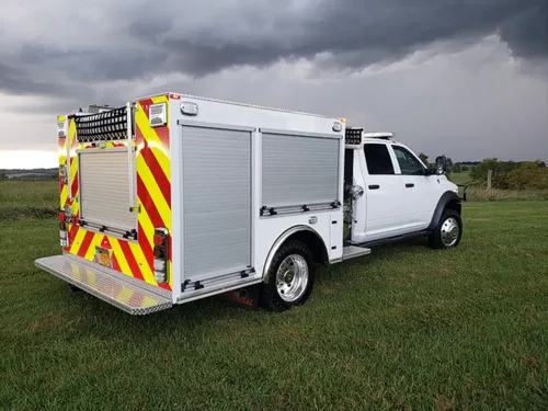 Exterior view of small fire truck showing cab, body compartments, and wheel/tire area.