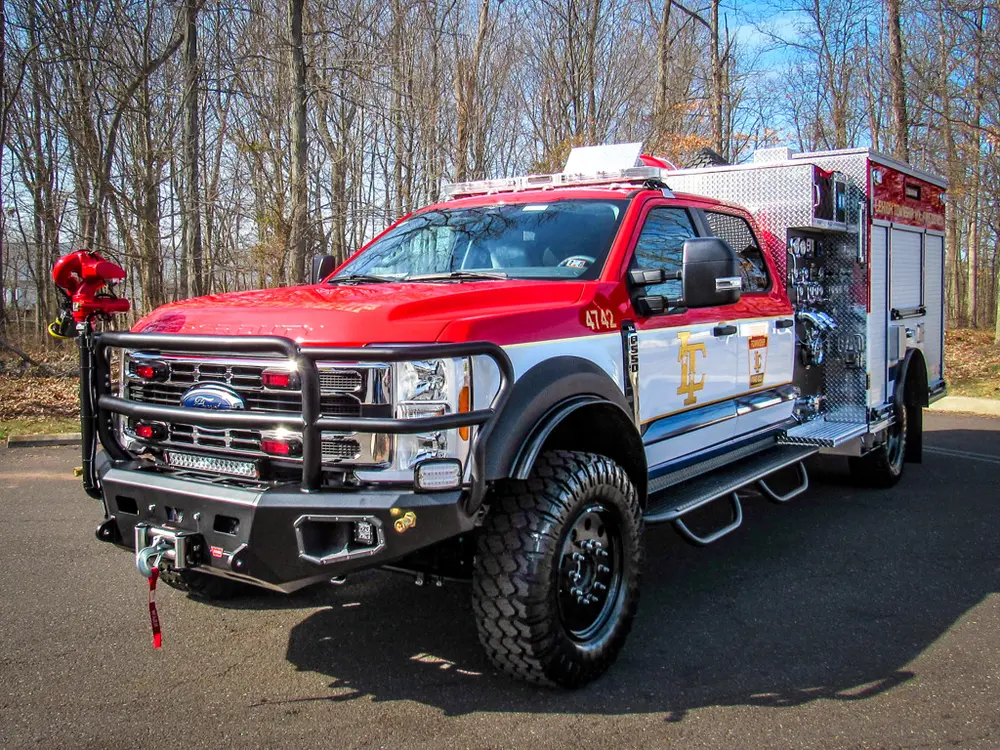 Exterior view of small fire truck showing cab, body compartments, and wheel/tire area.