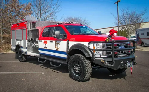 Exterior view of small fire truck showing cab, body compartments, and wheel/tire area.