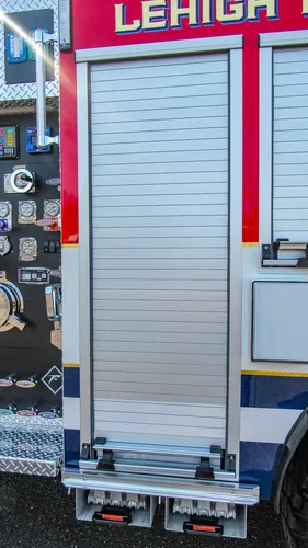 Exterior view of small fire truck showing cab, body compartments, and wheel/tire area.