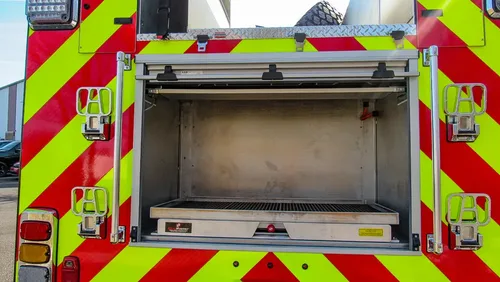 Exterior view of small fire truck showing cab, body compartments, and wheel/tire area.