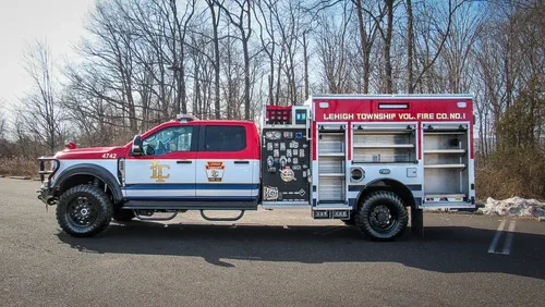 Exterior view of small fire truck showing cab, body compartments, and wheel/tire area.
