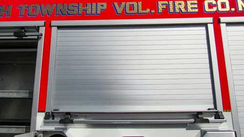 Exterior view of small fire truck showing cab, body compartments, and wheel/tire area.