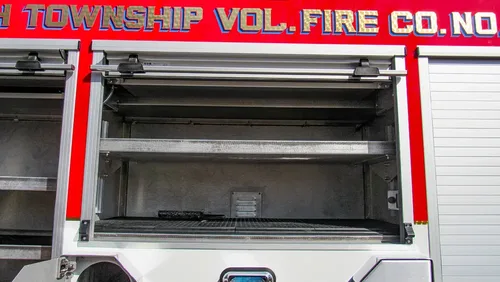 Exterior view of small fire truck showing cab, body compartments, and wheel/tire area.