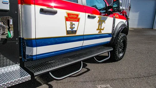 Exterior view of small fire truck showing cab, body compartments, and wheel/tire area.