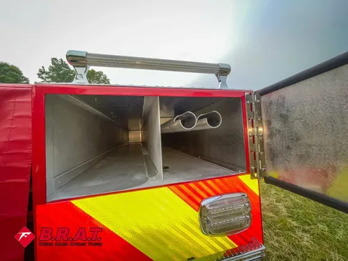 Exterior view of small fire truck showing cab, body compartments, and wheel/tire area.