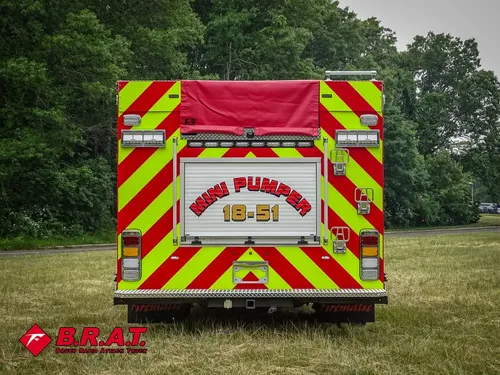 Exterior view of small fire truck showing cab, body compartments, and wheel/tire area.