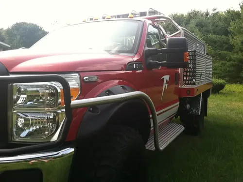 Exterior view of small fire truck showing cab, body compartments, and wheel/tire area.