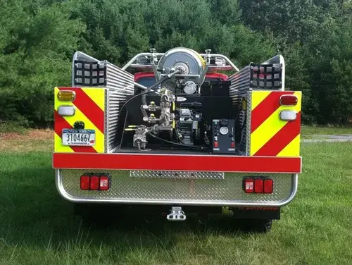 Exterior view of small fire truck showing cab, body compartments, and wheel/tire area.