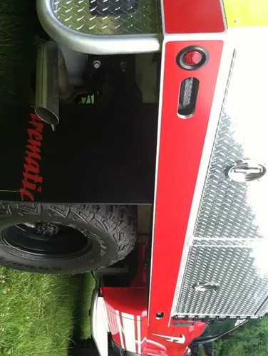 Exterior view of small fire truck showing cab, body compartments, and wheel/tire area.