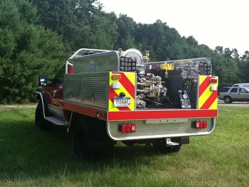 Exterior view of small fire truck showing cab, body compartments, and wheel/tire area.