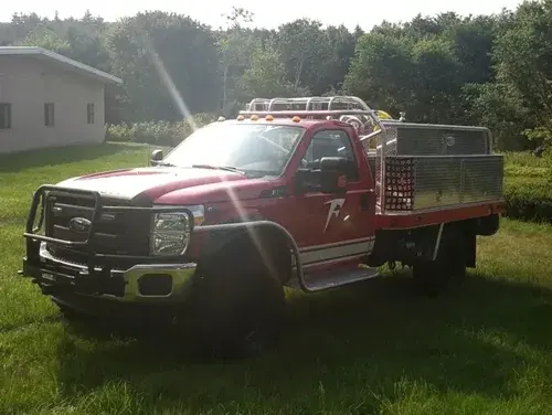 Exterior view of small fire truck showing cab, body compartments, and wheel/tire area.