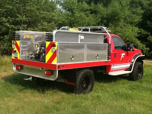 Exterior view of small fire truck showing cab, body compartments, and wheel/tire area.