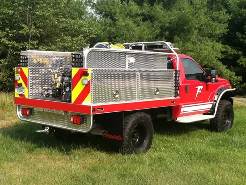 Exterior view of small fire truck showing cab, body compartments, and wheel/tire area.