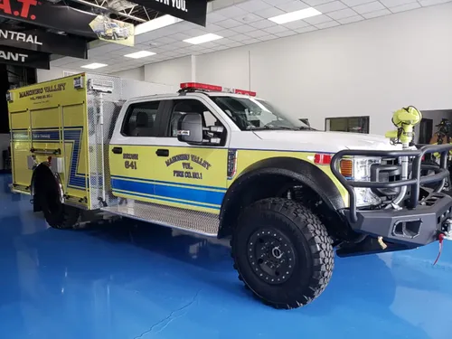 Exterior view of small fire truck showing cab, body compartments, and wheel/tire area.