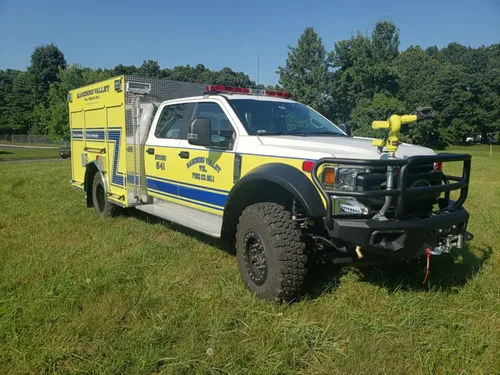 Exterior view of small fire truck showing cab, body compartments, and wheel/tire area.