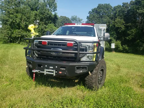 Exterior view of small fire truck showing cab, body compartments, and wheel/tire area.
