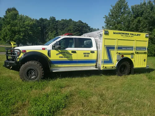 Exterior view of small fire truck showing cab, body compartments, and wheel/tire area.