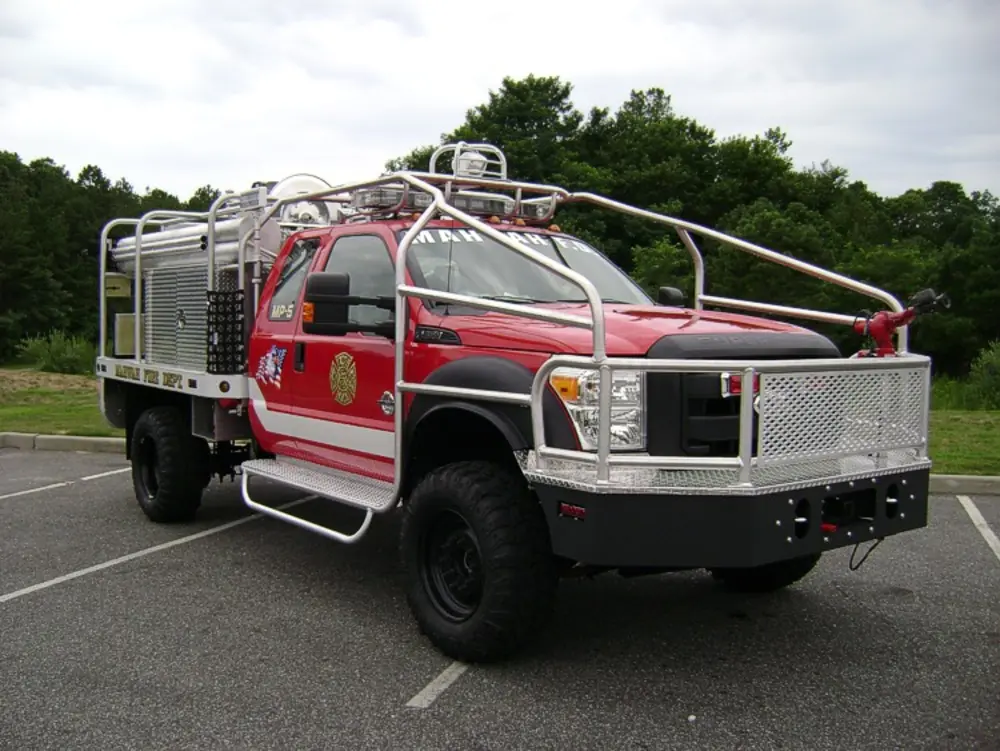 Exterior view of small fire truck showing cab, body compartments, and wheel/tire area.