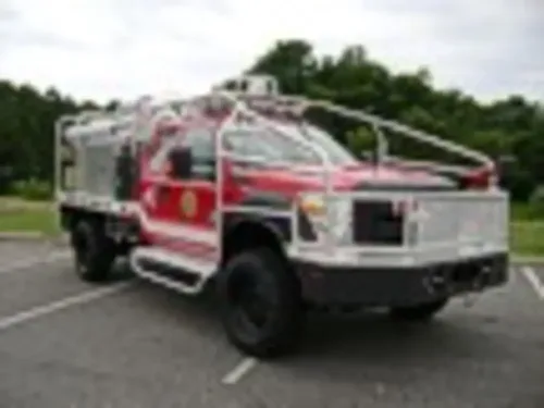 Exterior view of small fire truck showing cab, body compartments, and wheel/tire area.