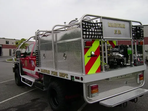 Exterior view of small fire truck showing cab, body compartments, and wheel/tire area.