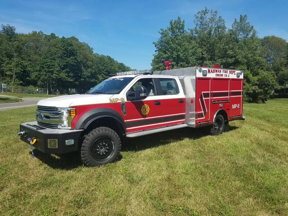 Exterior view of small fire truck showing cab, body compartments, and wheel/tire area.