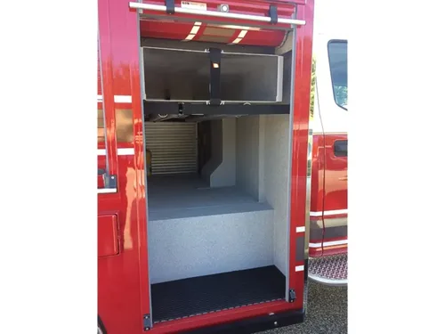 Exterior view of small fire truck showing cab, body compartments, and wheel/tire area.