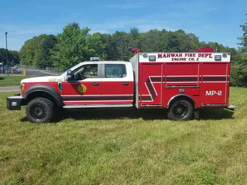 Exterior view of small fire truck showing cab, body compartments, and wheel/tire area.