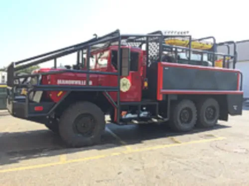 Exterior view of small fire truck showing cab, body compartments, and wheel/tire area.