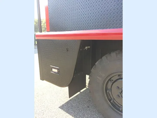 Exterior view of small fire truck showing cab, body compartments, and wheel/tire area.