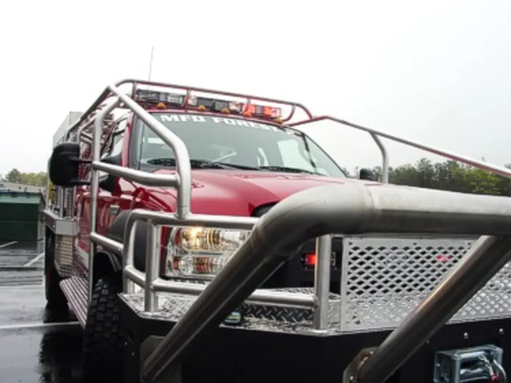Exterior view of small fire truck showing cab, body compartments, and wheel/tire area.