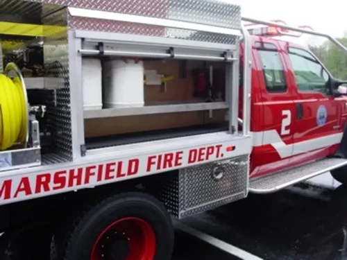 Exterior view of small fire truck showing cab, body compartments, and wheel/tire area.