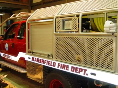 Exterior view of small fire truck showing cab, body compartments, and wheel/tire area.