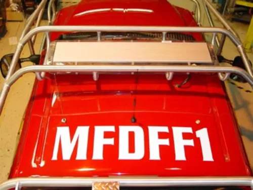 Exterior view of small fire truck showing cab, body compartments, and wheel/tire area.
