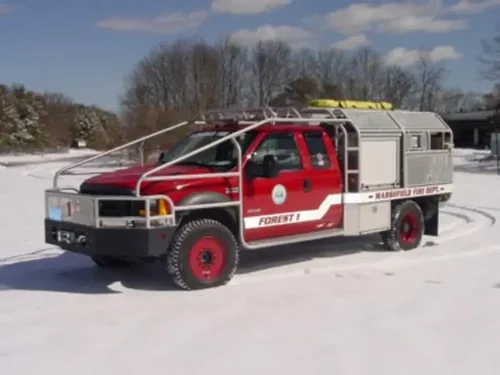Exterior view of small fire truck showing cab, body compartments, and wheel/tire area.