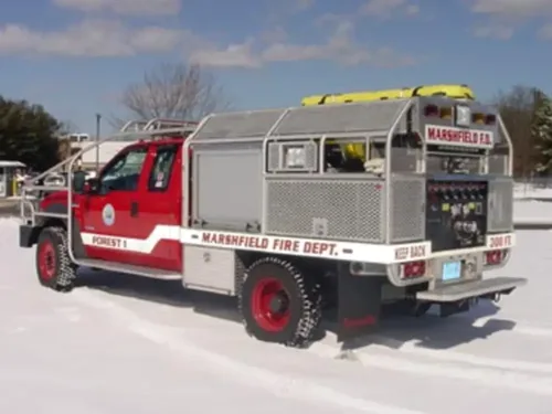 Exterior view of small fire truck showing cab, body compartments, and wheel/tire area.