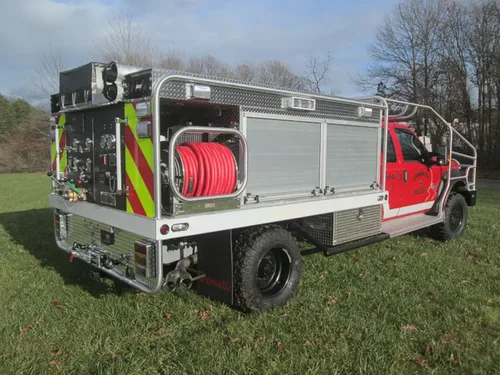Exterior view of small fire truck showing cab, body compartments, and wheel/tire area.
