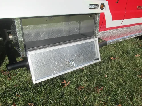 Exterior view of small fire truck showing cab, body compartments, and wheel/tire area.