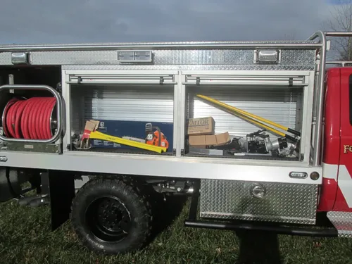 Exterior view of small fire truck showing cab, body compartments, and wheel/tire area.