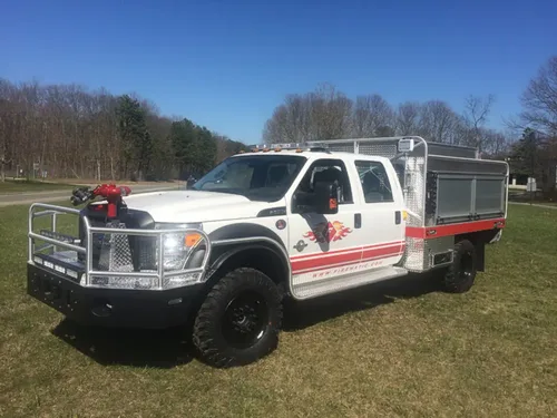 Exterior view of small fire truck showing cab, body compartments, and wheel/tire area.