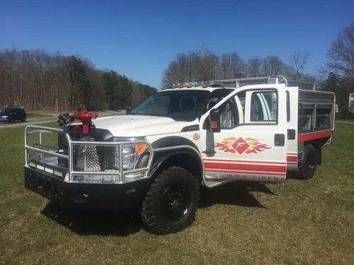 Exterior view of small fire truck showing cab, body compartments, and wheel/tire area.