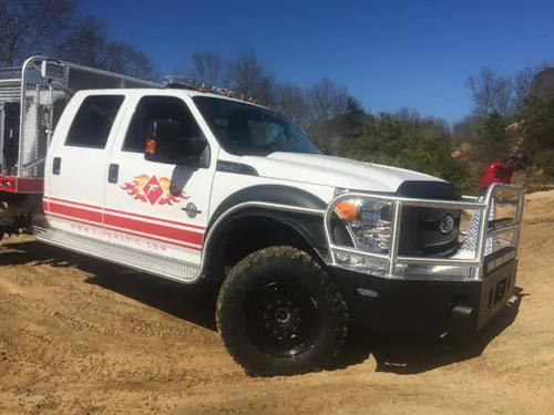 Exterior view of small fire truck showing cab, body compartments, and wheel/tire area.