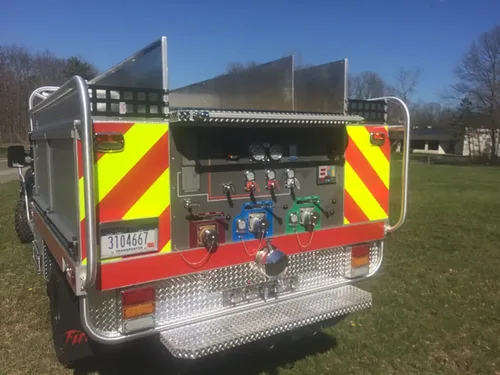 Exterior view of small fire truck showing cab, body compartments, and wheel/tire area.