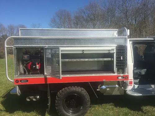 Exterior view of small fire truck showing cab, body compartments, and wheel/tire area.