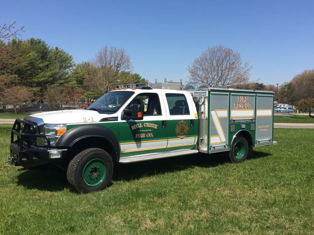 Exterior view of small fire truck showing cab, body compartments, and wheel/tire area.